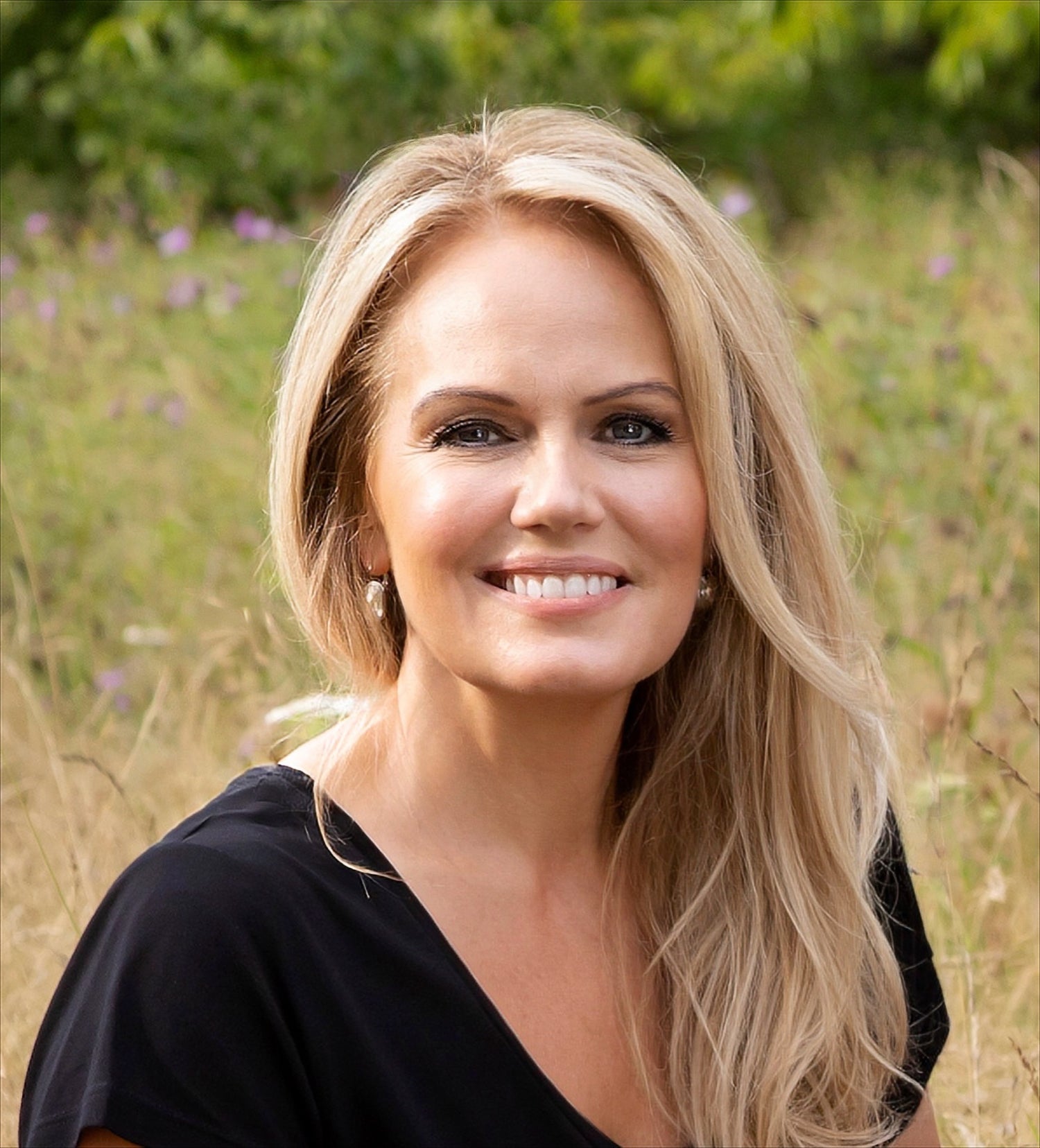 Woman with blonde hair standing in a field with greenery and flowers in the background